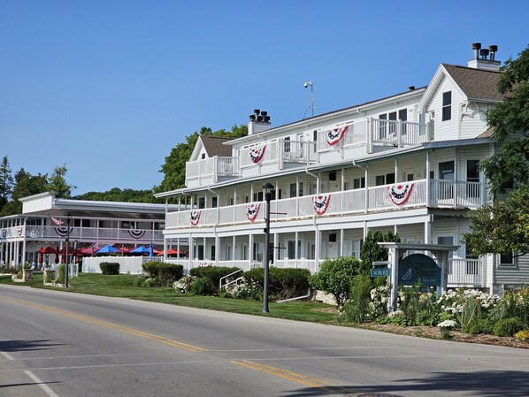 A two-story white building with balconies, a covered front porch, and American flags.