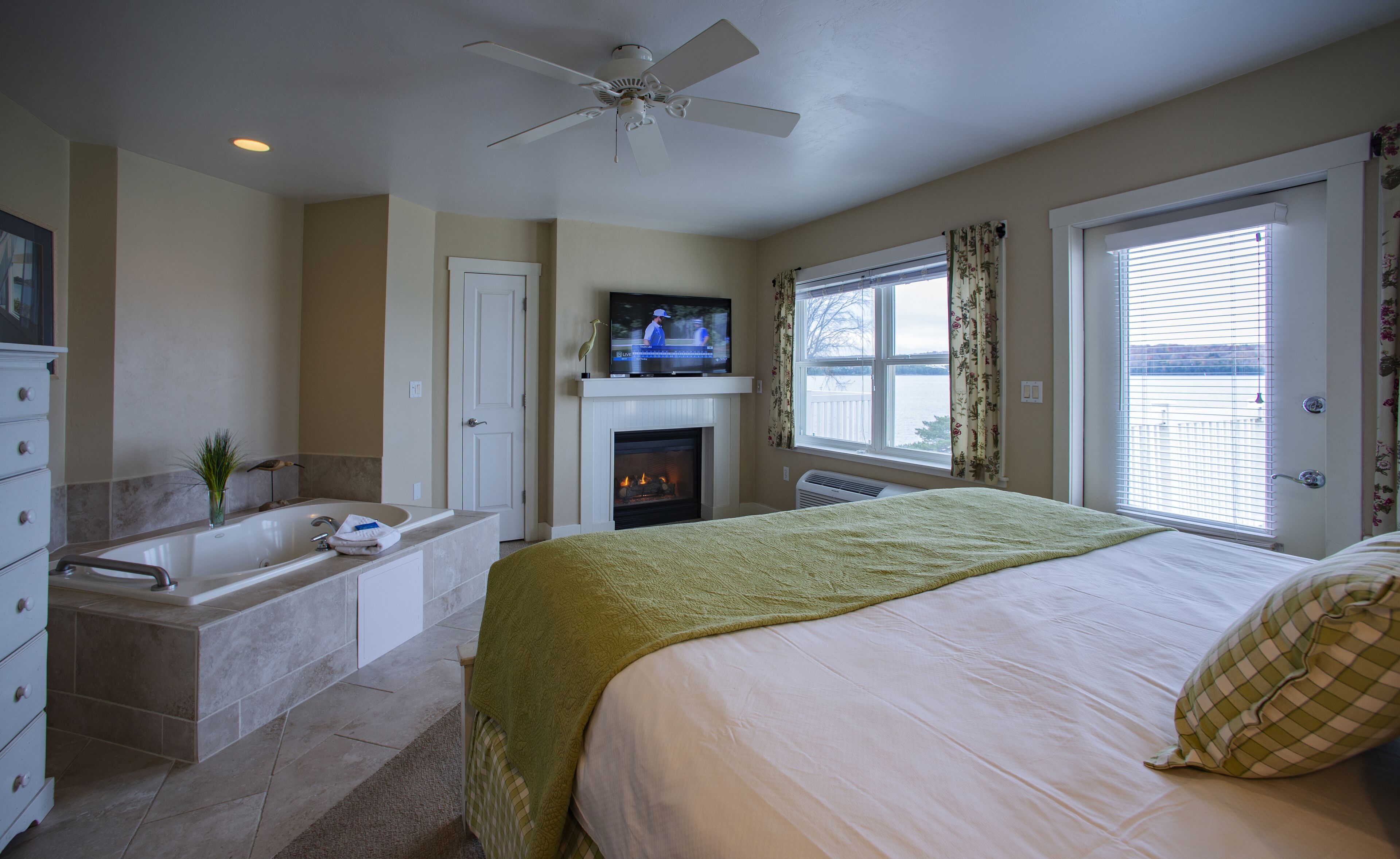 A bedroom with a bed, a television, a fireplace, a bathtub, and a window with blinds.