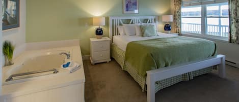 Une chambre avec un grand lit, une table de chevet, une petite table de nuit avec une lampe, une fenêtre avec des rideaux et un ventilateur de plafond.