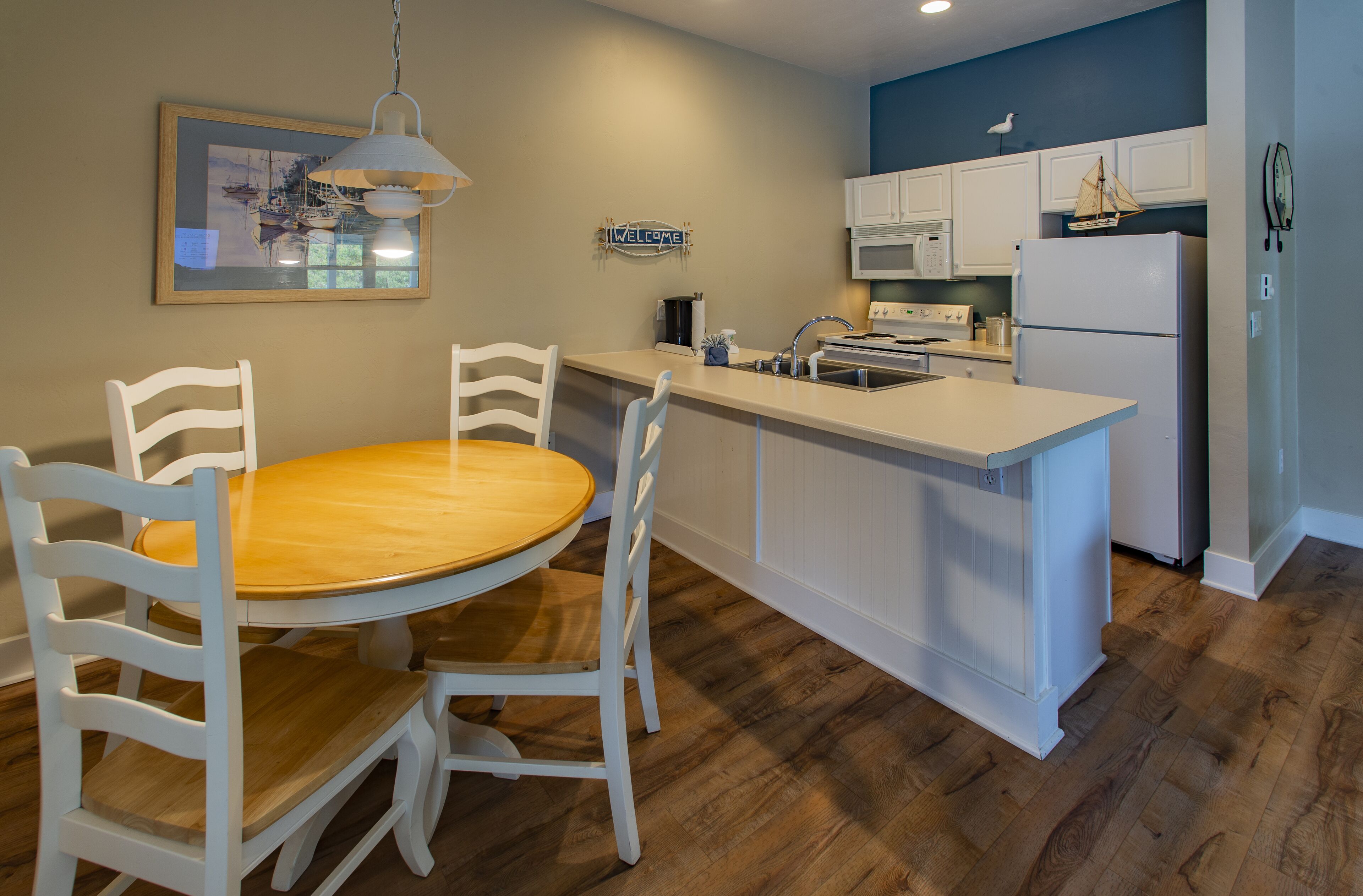 Una cocina con una mesa de comedor de madera, sillas blancas, una isla blanca con un fregadero y un microondas sobre la estufa.