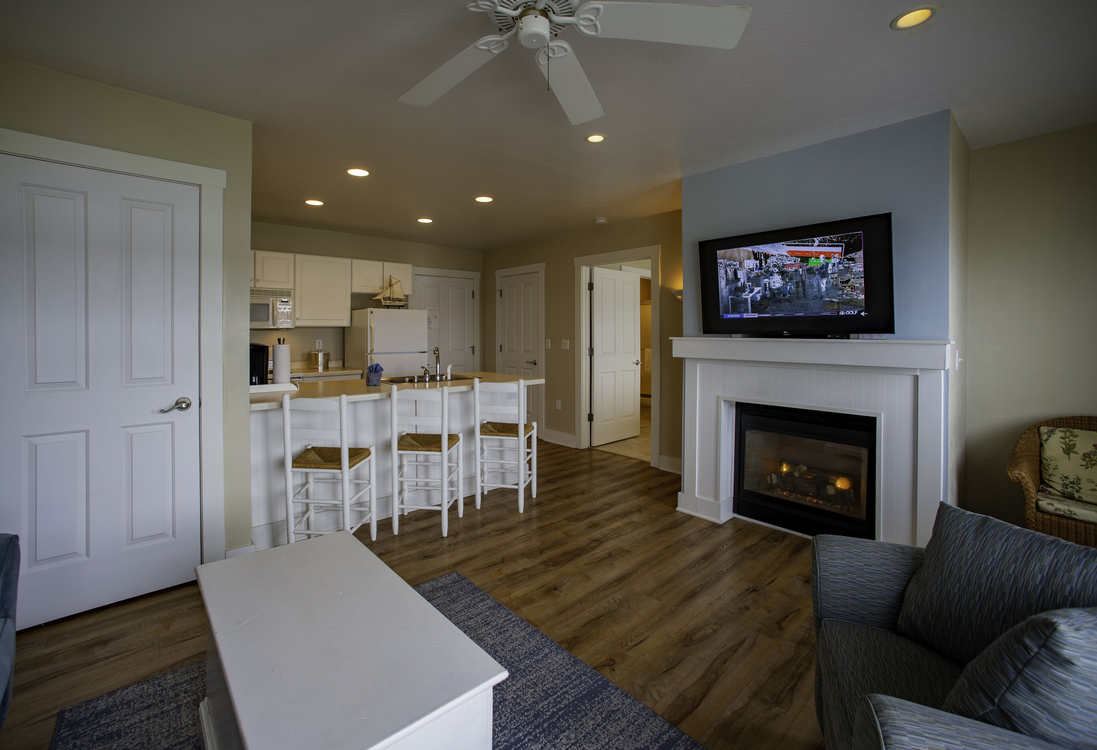 A living room with a fireplace, a television, and a kitchen in the background.
