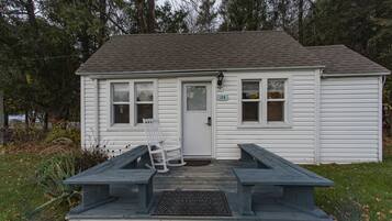 A small white building with a porch, a rocking chair, and a welcome mat.