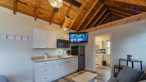 A modern kitchen with white cabinets, a microwave, and a refrigerator. There is a television mounted above the counter.