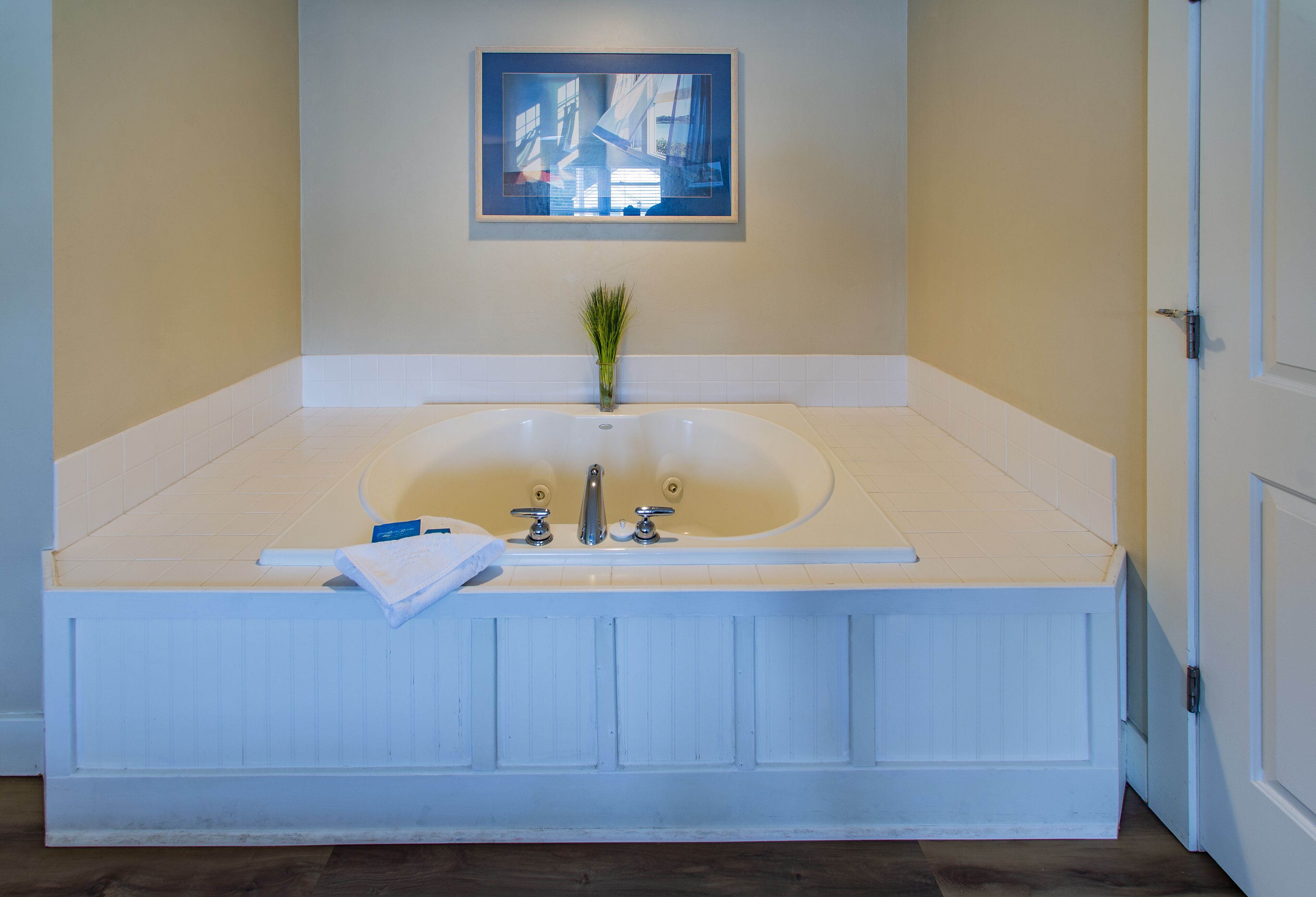 Une grande baignoire avec une petite plante au centre, une serviette sur le bord et un tableau encadré au-dessus de la baignoire.