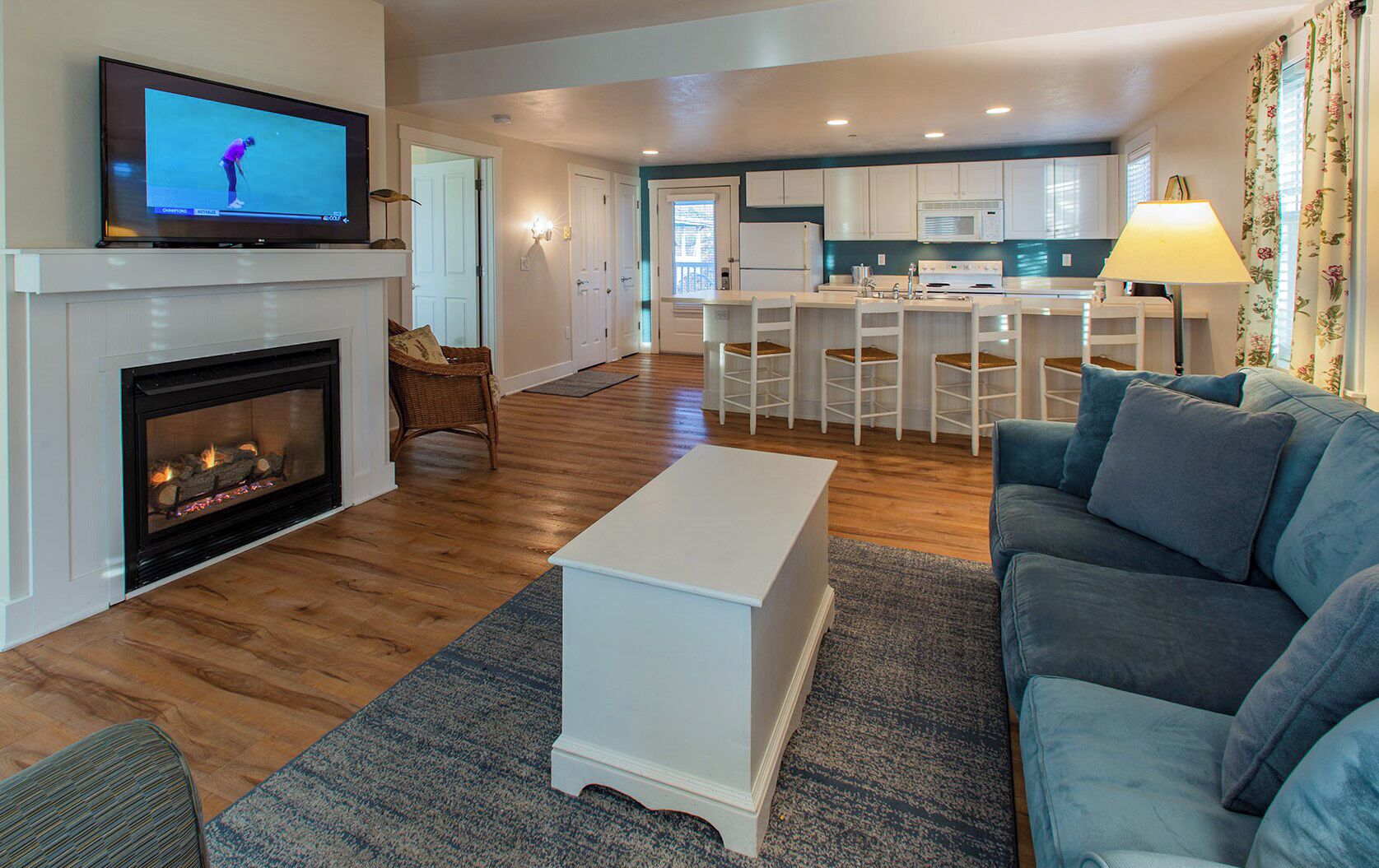 Una sala de estar con chimenea, televisor, sofá y una cocina al fondo.