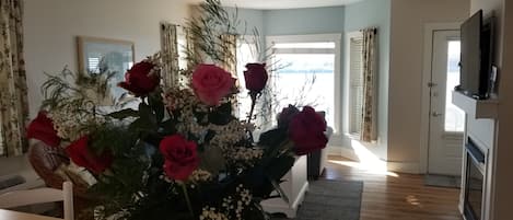 A living room with a dining table, a vase with flowers, a television, and a door leading to another room.