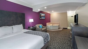 Habitación de hotel con una cama grande, una zona de estar con una silla, una bañera, un escritorio y un televisor.