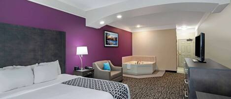 A hotel room with a large bed, a sitting area with a chair, a bathtub, a desk, and a television.