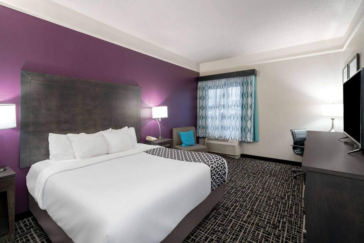 Hotelkamer met een groot bed, bureau, stoel, televisie, lamp en raam met gordijnen.