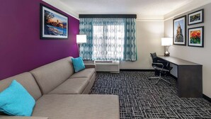 Habitación de hotel con pared morada, sofá color beige, escritorio con silla y alfombra estampada.