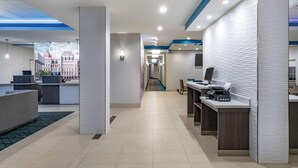 Un moderno vestíbulo de hotel con una recepción, zona de estar y vistas a un paisaje urbano a través de un tragaluz.