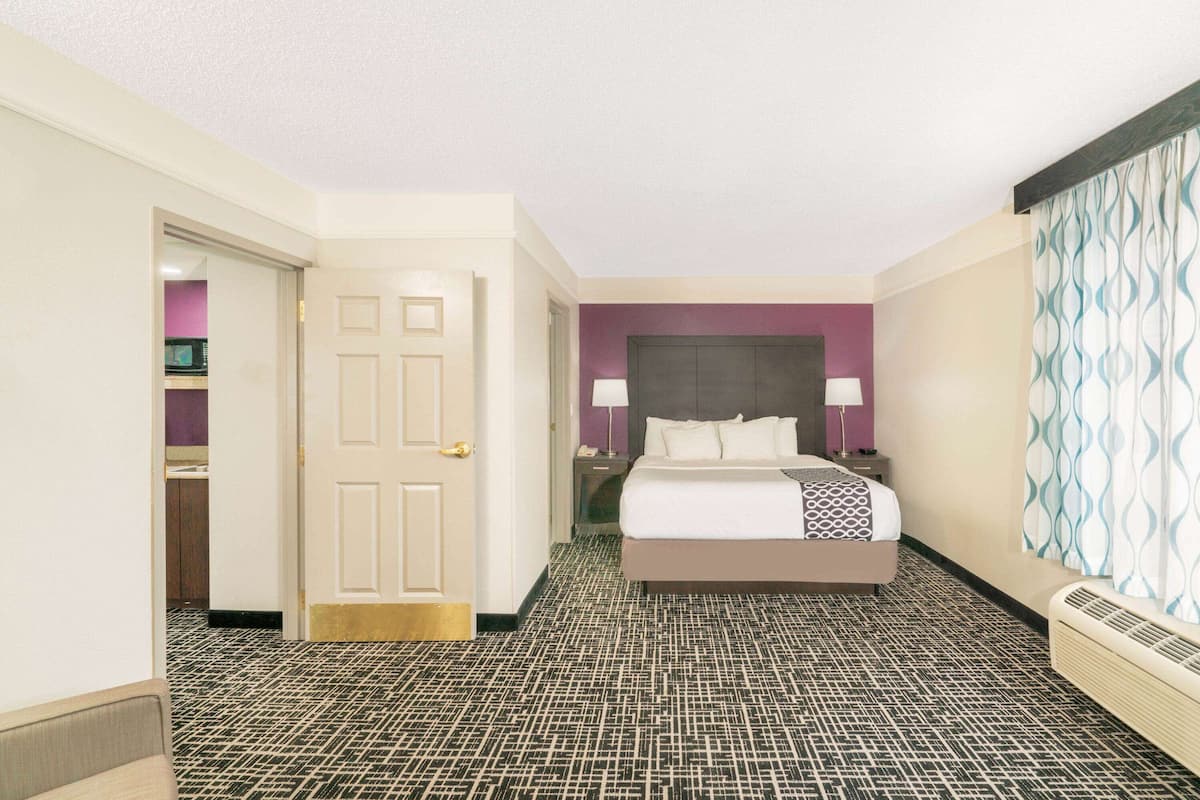 Een hotelkamer met een bed, een nachtkastje, een deur en een kamerbreed tapijt met een patroon.