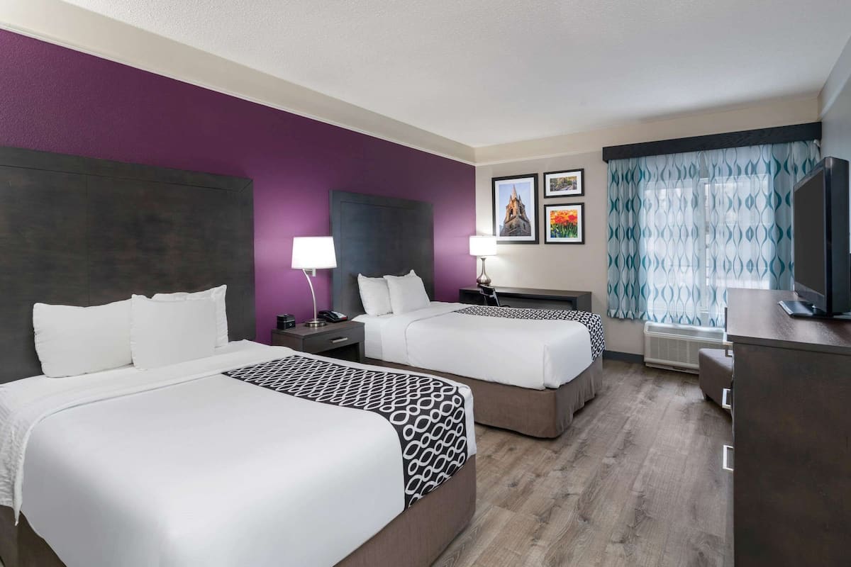 Een hotelkamer met twee bedden, een televisie, een bureau en een raam met gordijnen.