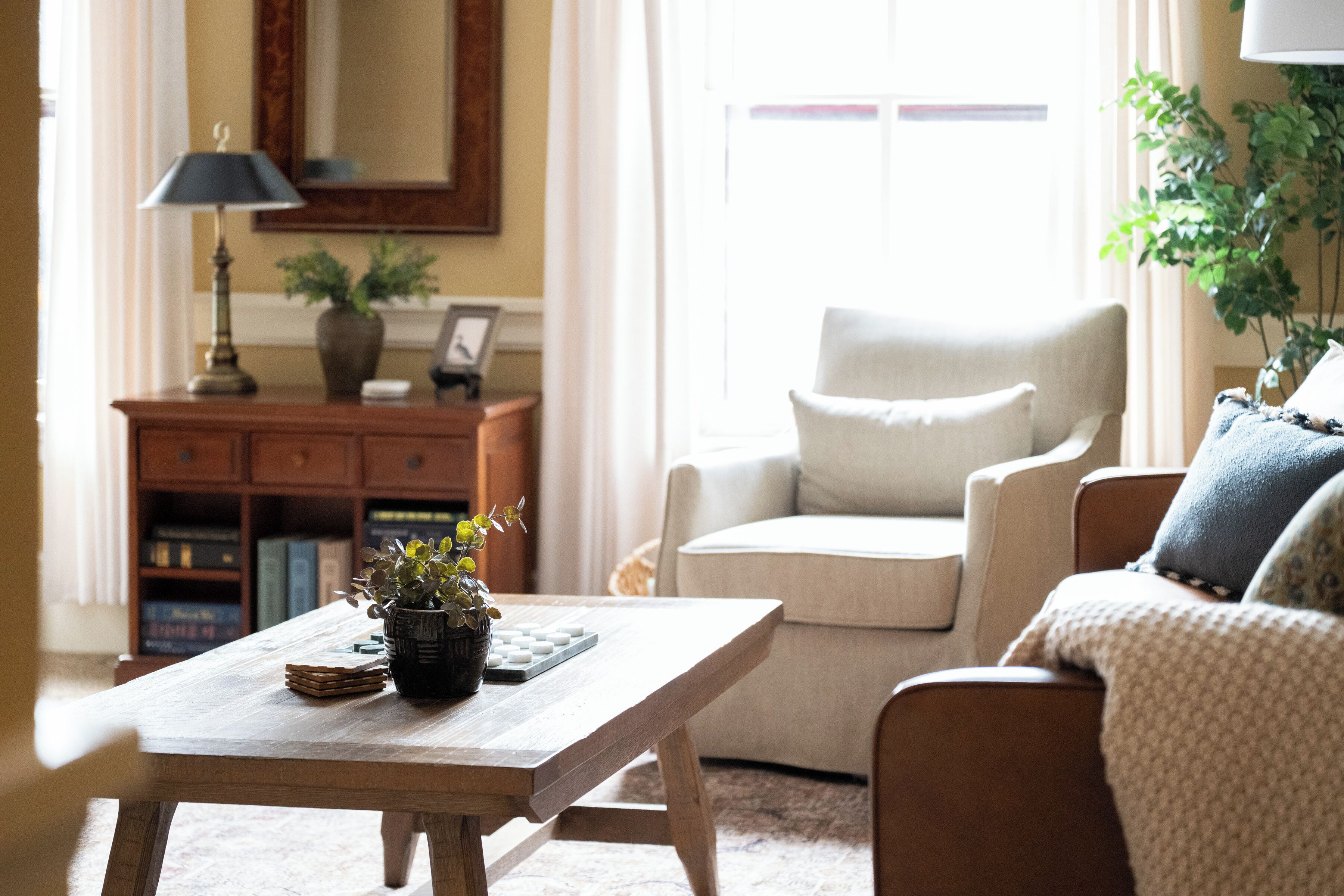 Una sala de estar con una mesa de centro de madera, un sofá, una silla, una lámpara y una estantería.