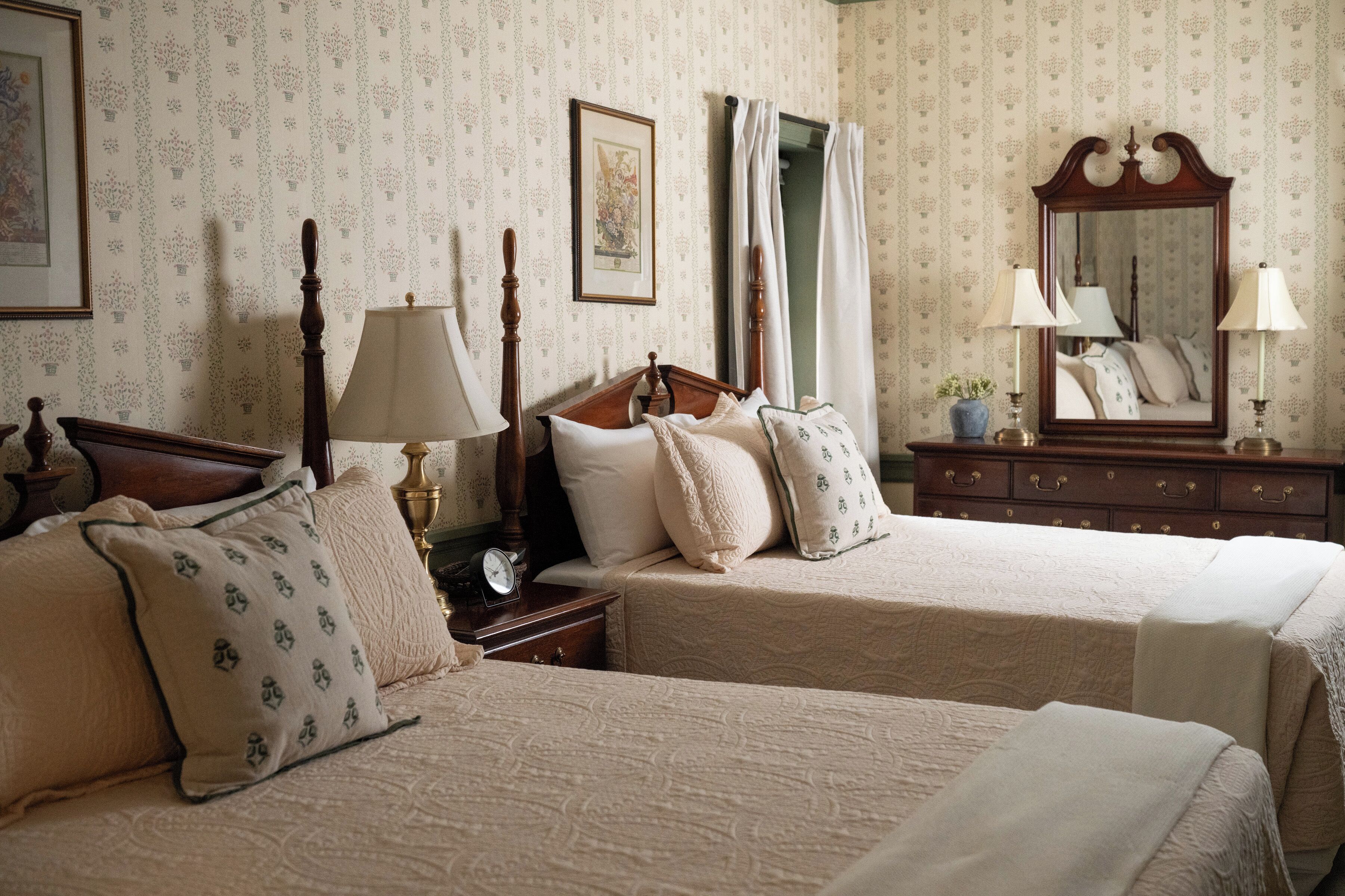 A bedroom with two beds, a nightstand, a dresser, a mirror, and a window with curtains.
