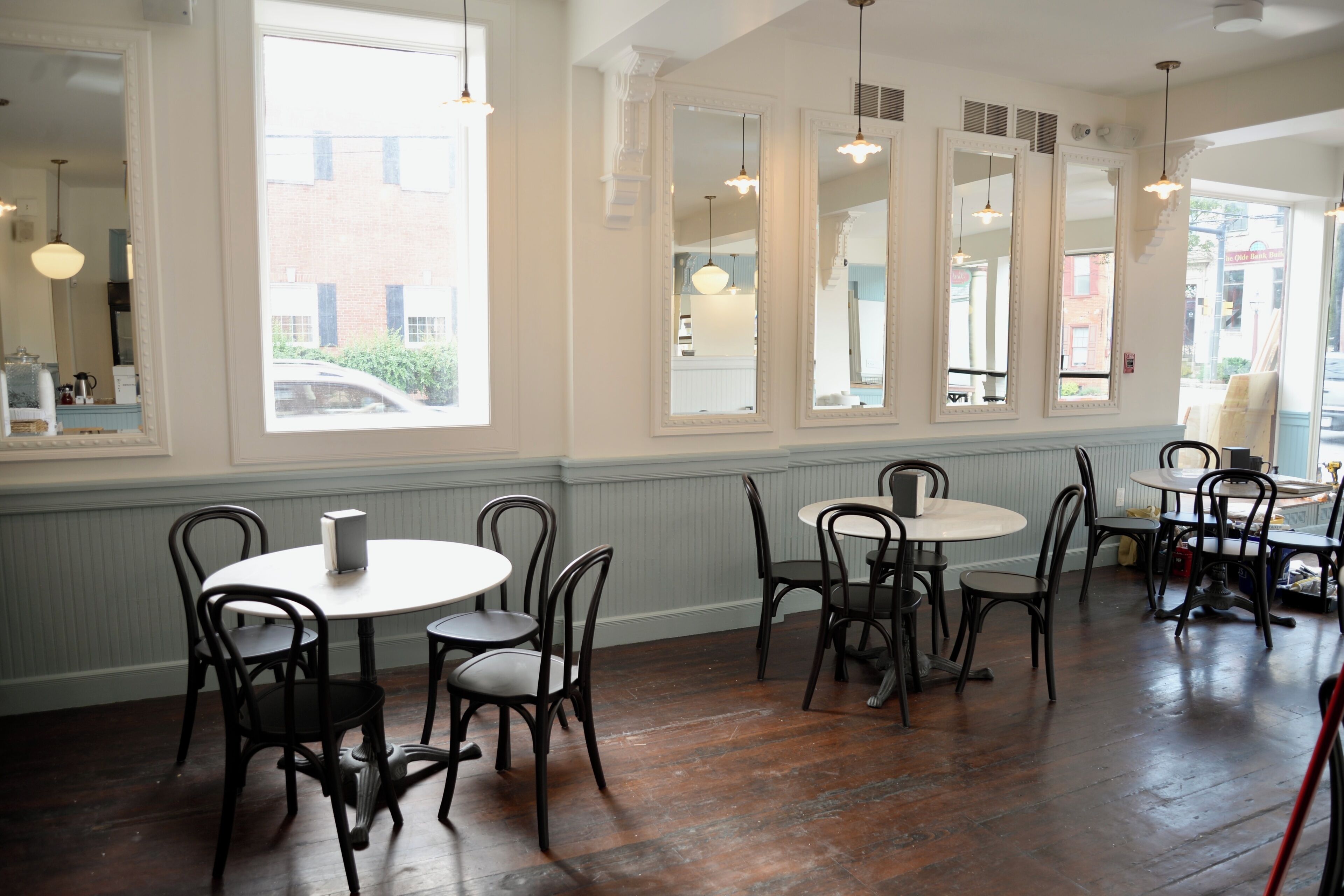 A dining area with round tables and chairs, large windows, and mirrors on the walls.