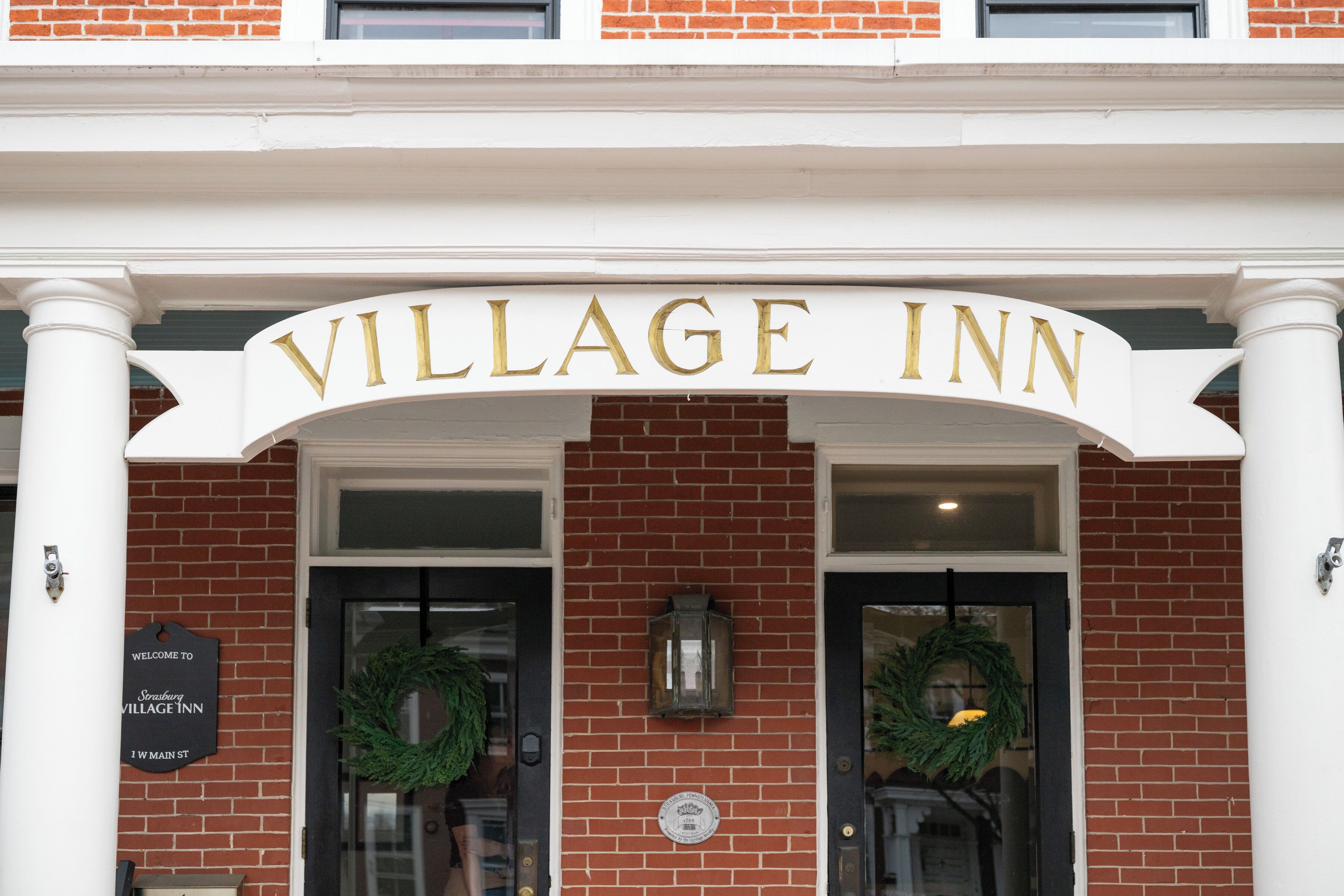 Un bâtiment en briques surmonté d’une arche blanche au-dessus de l’entrée, sur laquelle on peut lire l’inscription « VILLAGE INN ».