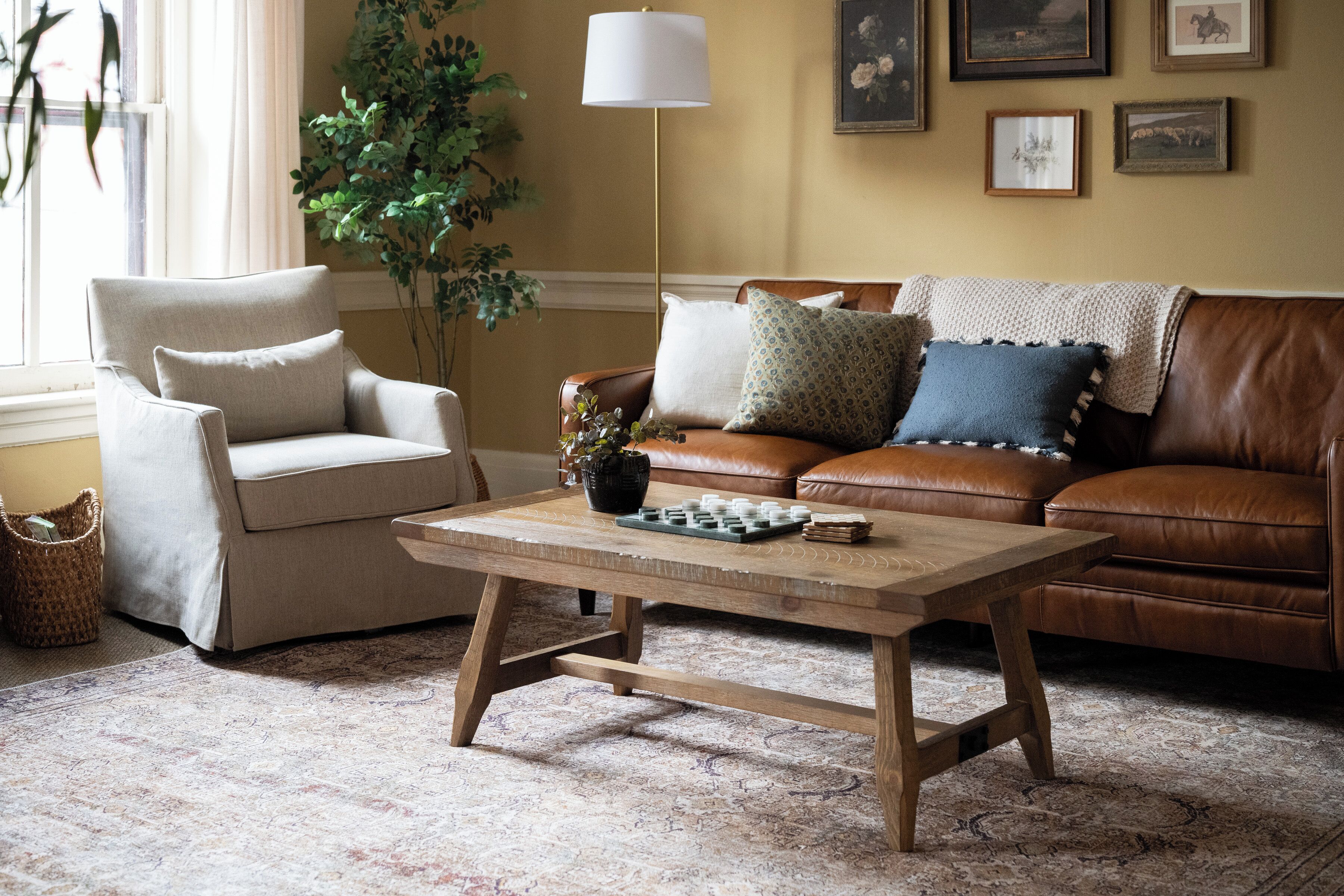 En stue med en beige lænestol, en brun lædersofa, et træsofabord og en tæppe med et mønster.
