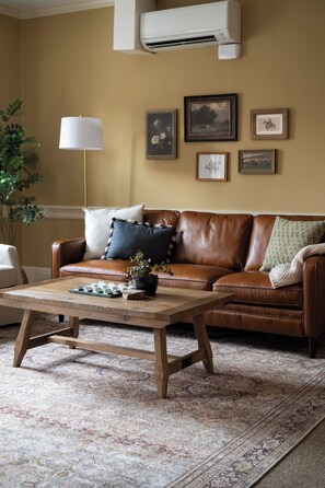 A living room with a brown leather sofa, a wooden coffee table, and a patterned rug. - Strasburg Village Inn (Strasburg)