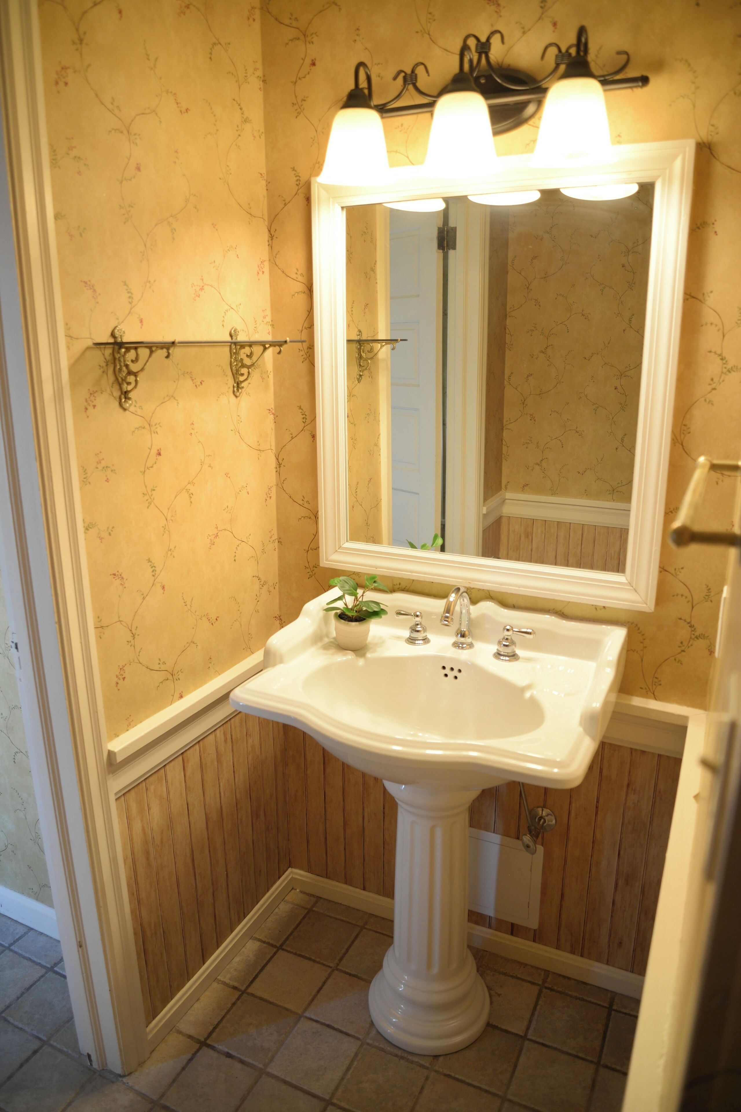 A bathroom with a pedestal sink, a mirror, and wall-mounted sconces.