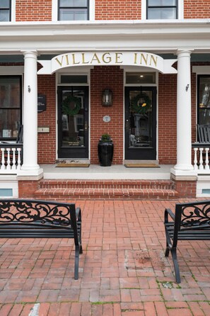 A brick building with a white entrance and the name 'Village Inn' above the doors. There are two black benches in front of the entrance. - Strasburg Village Inn (Strasburg)