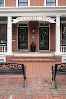 Un edificio de ladrillo con una entrada blanca y el nombre 'Village Inn' sobre las puertas. Hay dos bancos negros frente a la entrada.