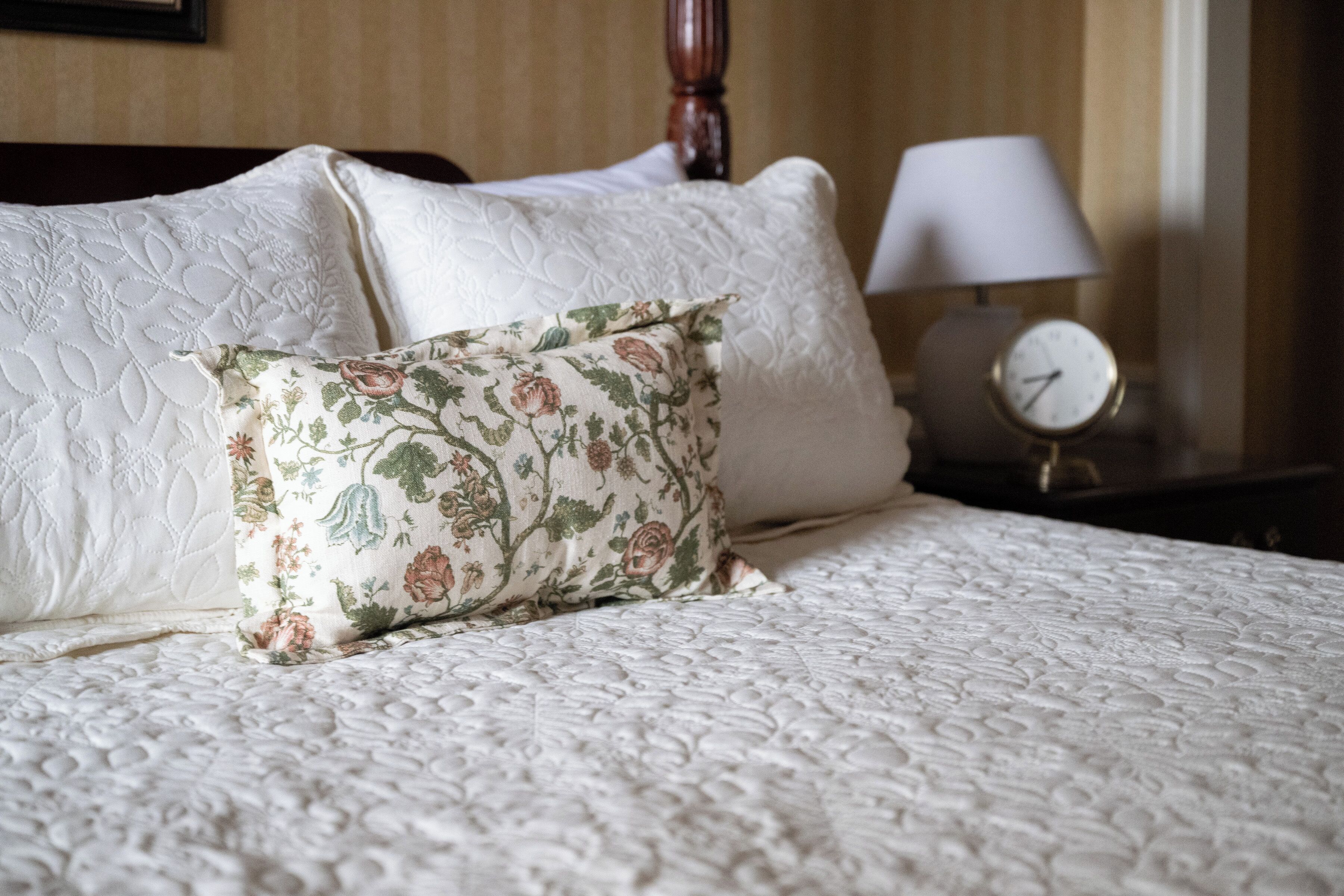 A neatly made bed with a floral pillow and a white textured bedspread.