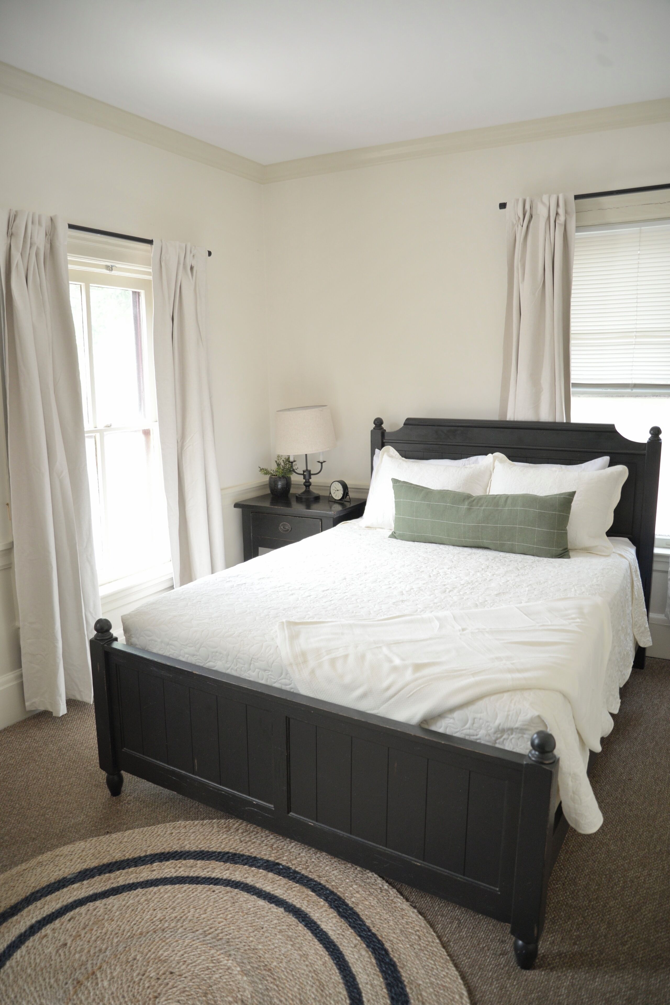 A bedroom with a large bed, a nightstand with a lamp, and a window with curtains.