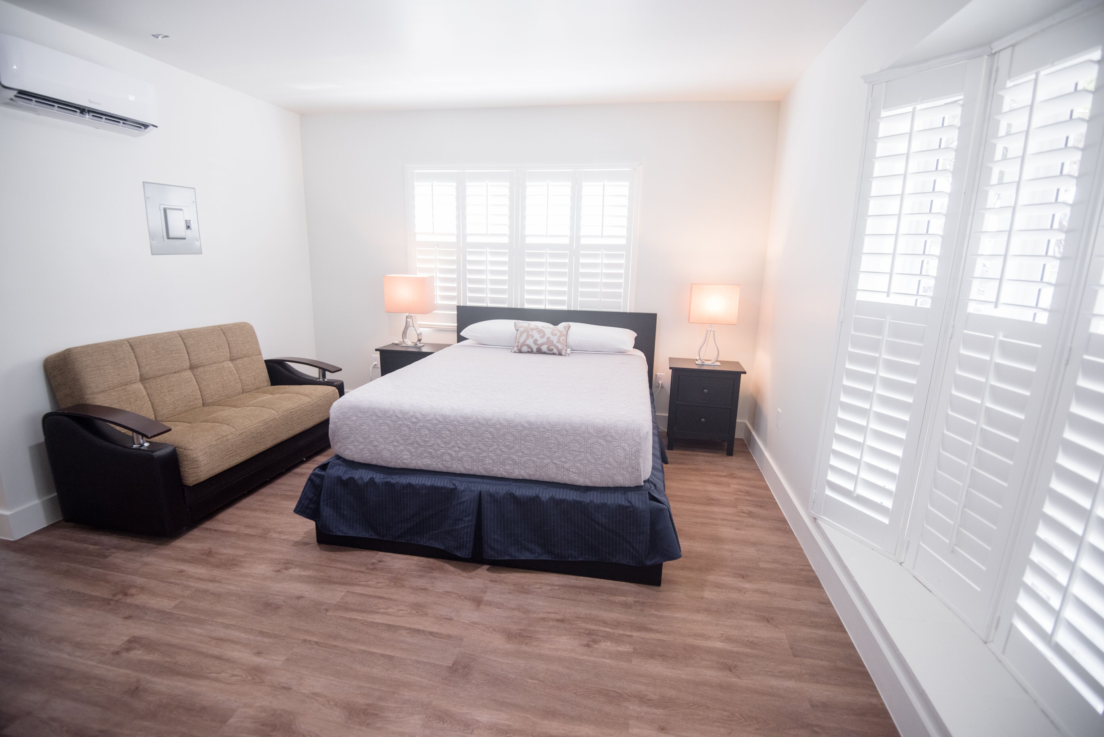 A bedroom with a bed, bedside tables, a sofa, and a window with blinds.