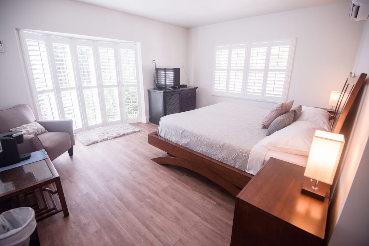 A modern bedroom with a large bed, a TV on a dresser, and a desk with a lamp.