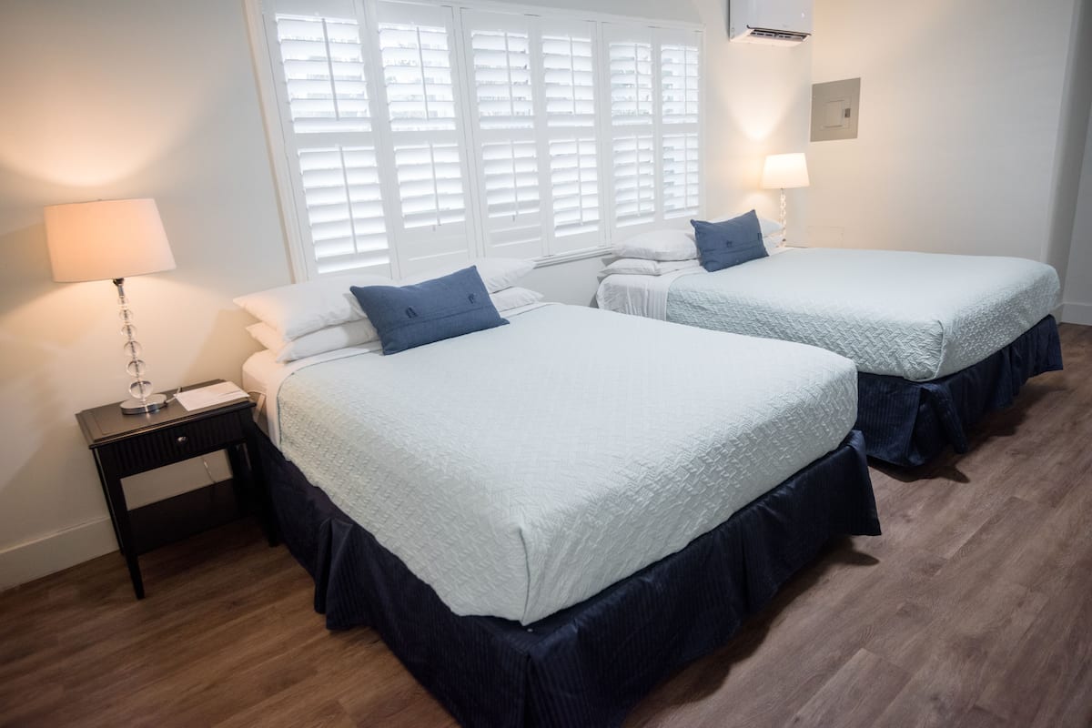 A bedroom with two beds, a nightstand, a lamp, and a window with blinds.