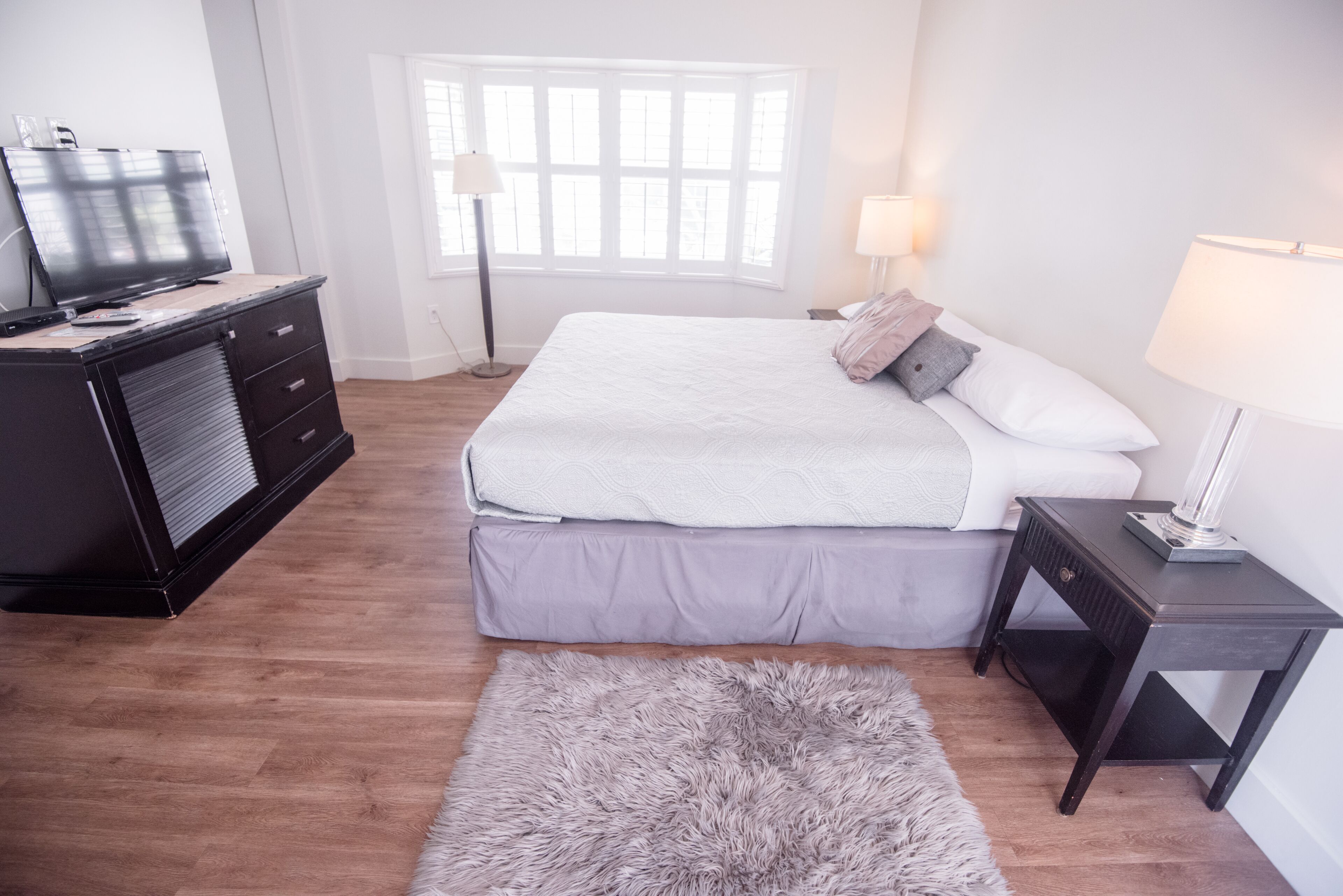 A bedroom with a bed, a dresser, a TV, and a lamp.