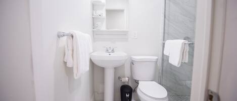 A compact bathroom with a white sink, toilet, and glass shower enclosure.