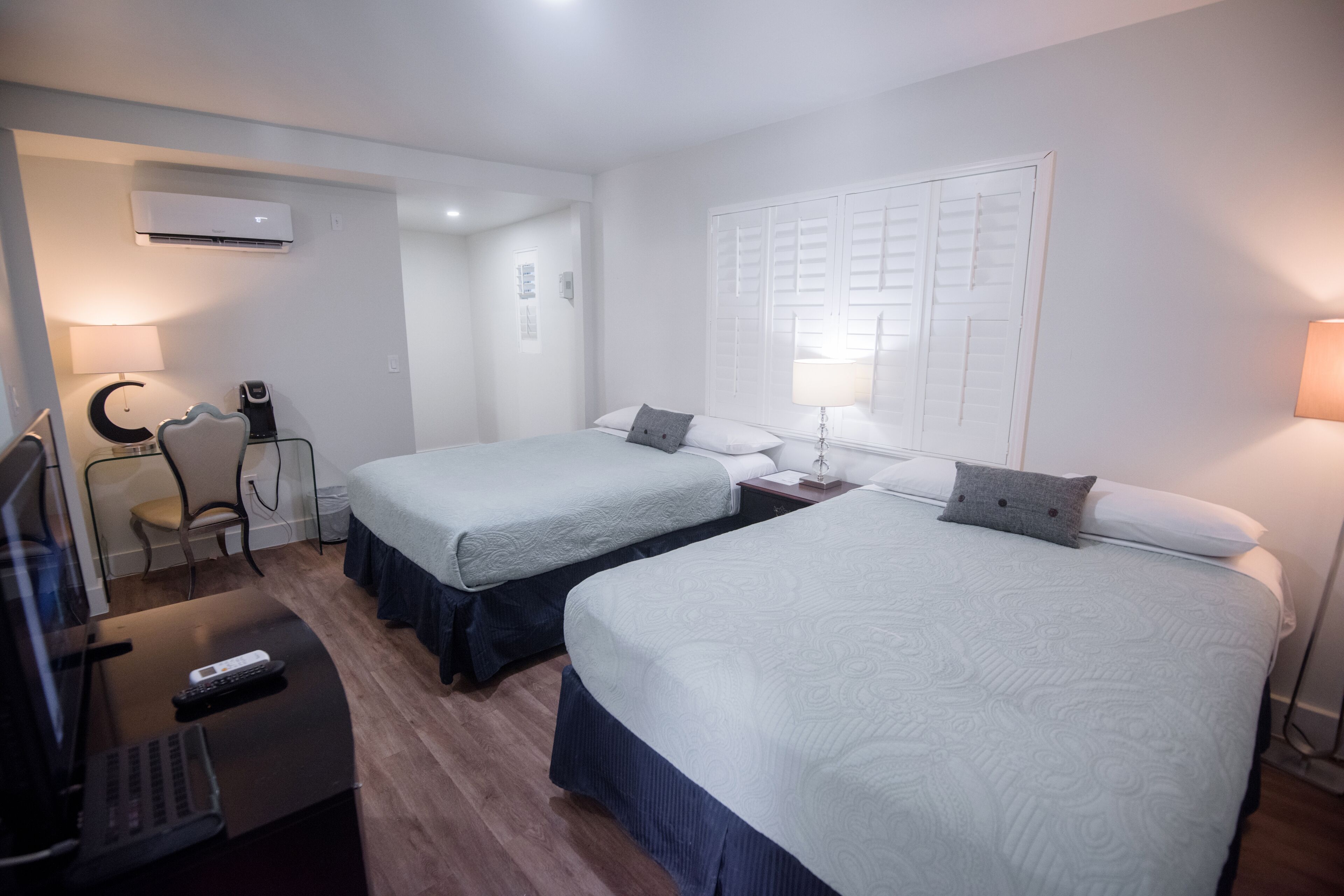 A hotel room with two single beds, a desk with a laptop and remote control, a chair, and a desk lamp.
