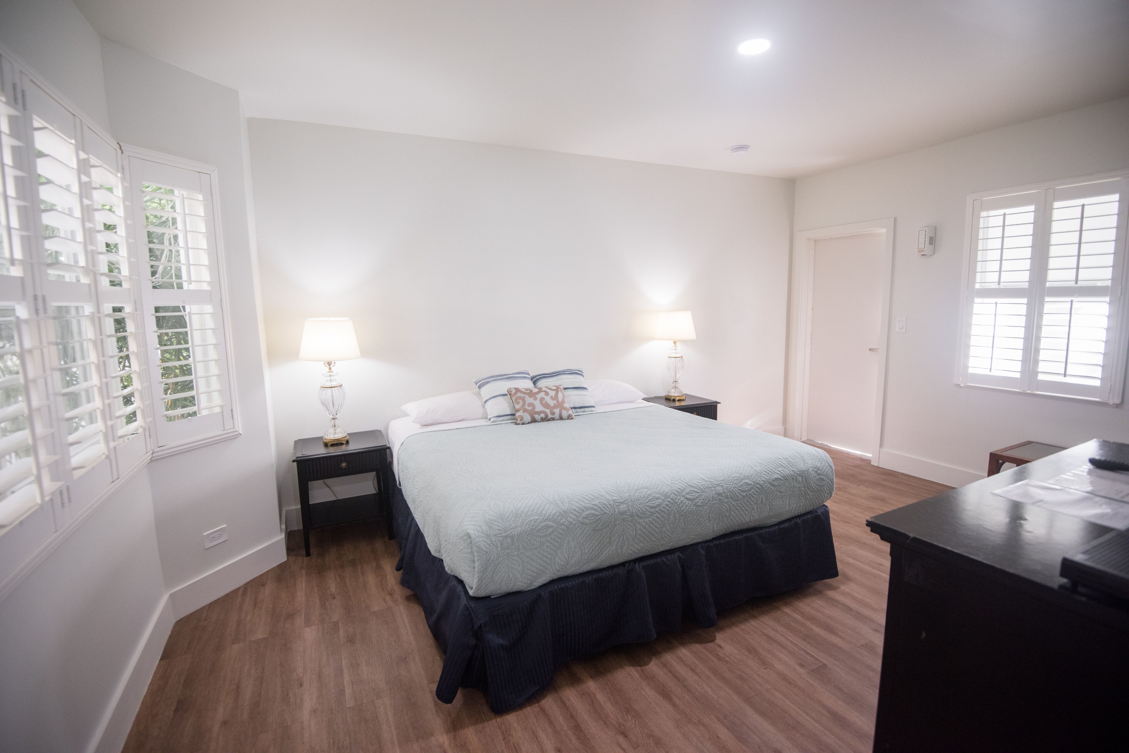 A bedroom with a bed, two bedside tables, a desk, and a window with blinds.