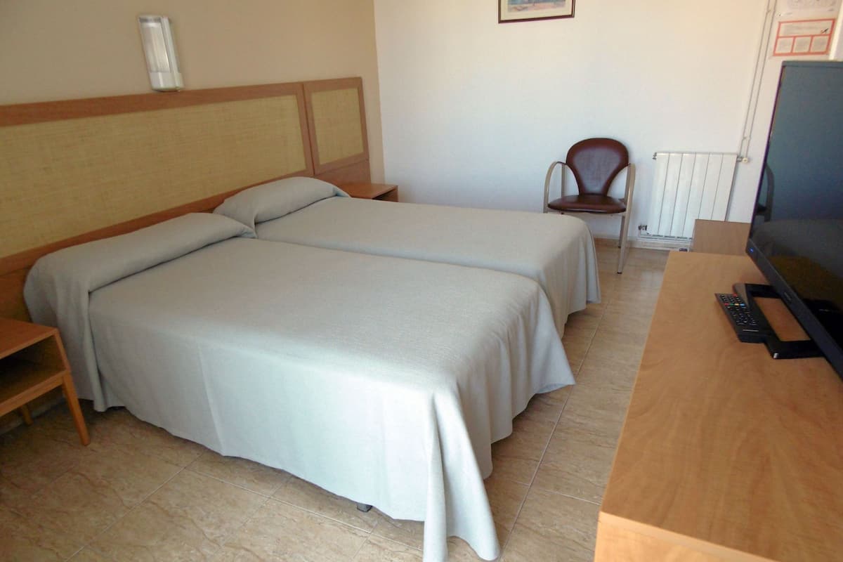 A hotel room with two beds, a wooden desk, a television, and a chair.