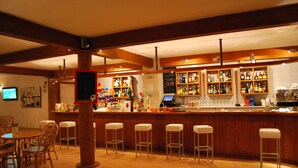 A bar area with wooden beams, a counter with various bottles, and bar stools. - Hotel Apartamentos Solimar (Calafell)