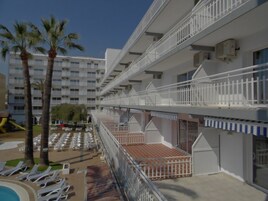 Un hotel con varias terrazas, una zona de piscina con tumbonas y palmeras.