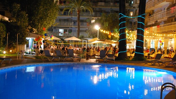 A pool area with lounge chairs and umbrellas, surrounded by buildings and trees. - Hotel Apartamentos Solimar (Calafell)