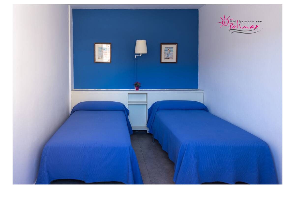 A room with two single beds, a nightstand, a lamp, and two framed pictures on the wall.