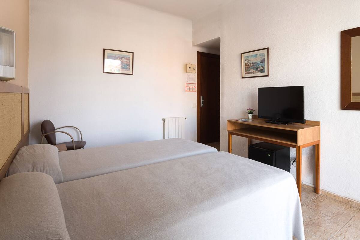 A hotel room with a bed, a desk with a television, and a chair.
