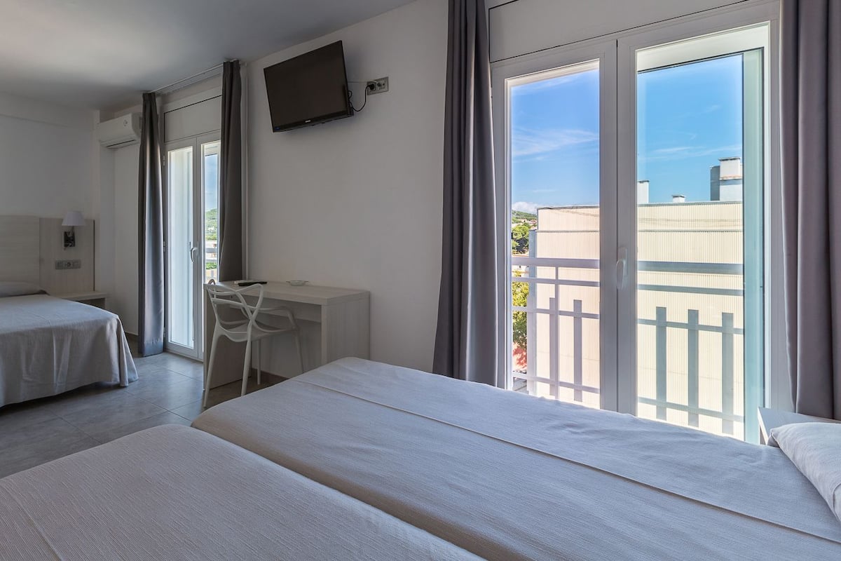 A hotel room with two beds, a desk, a chair, and a TV.