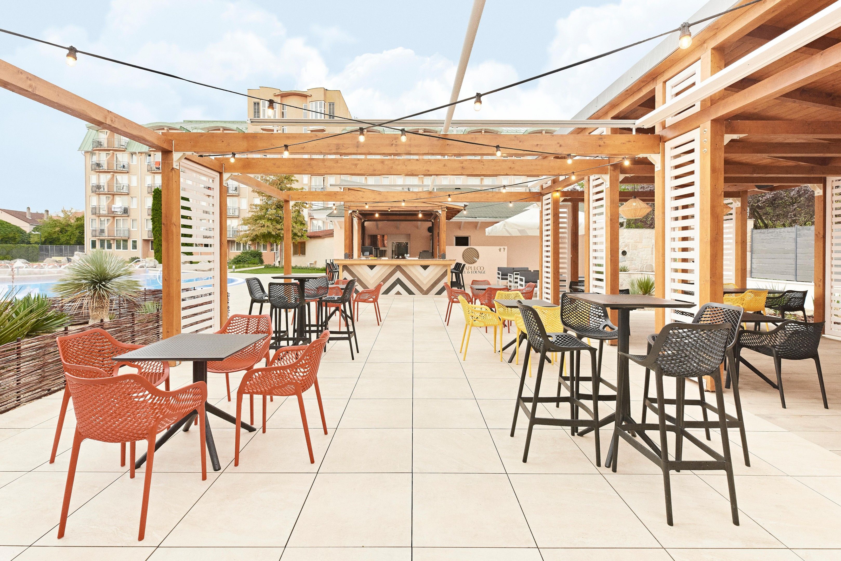 Un patio al aire libre con varias mesas y sillas, una zona de bar y vistas a un edificio al fondo.