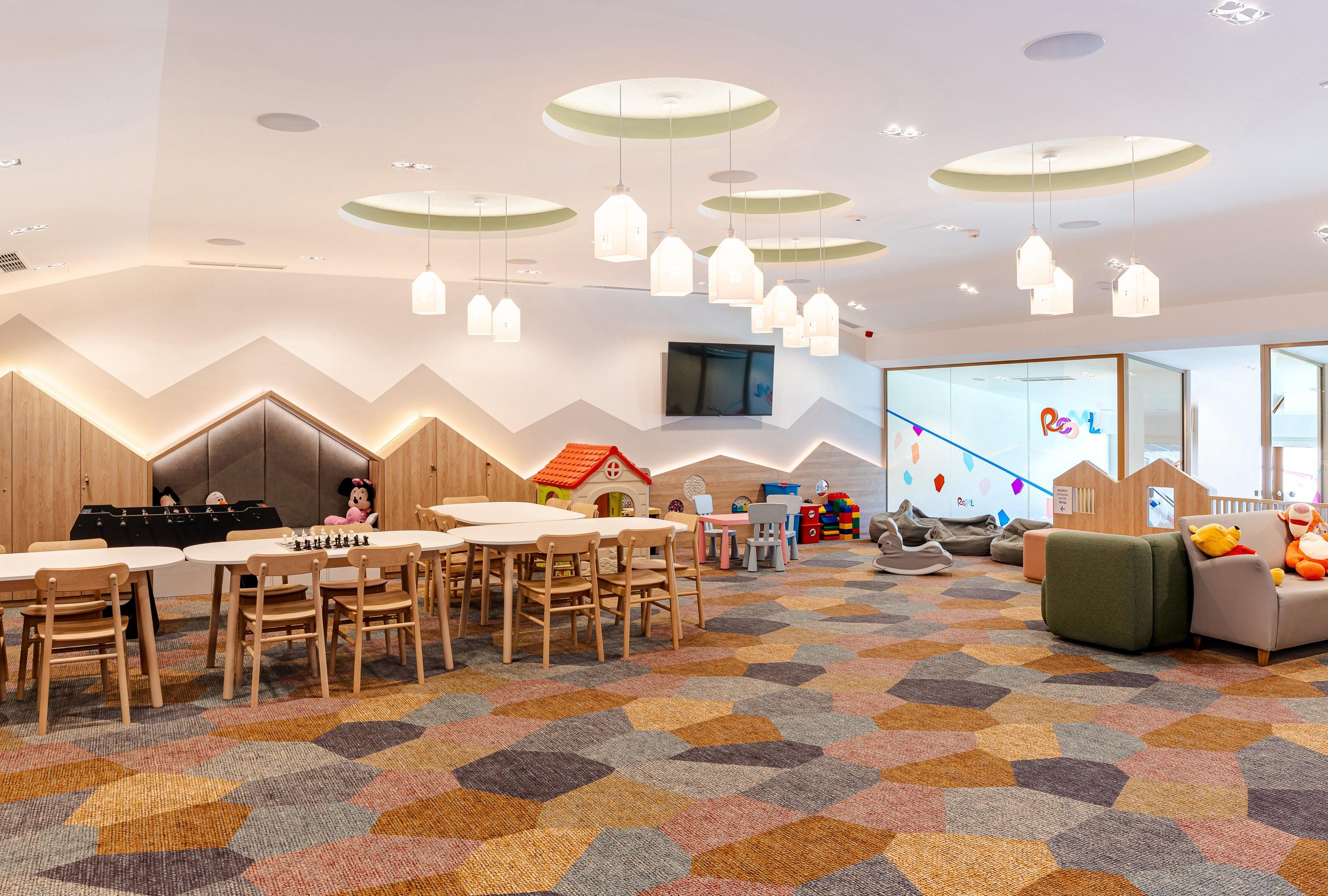 Zona de juegos infantiles con mesas, sillas y una alfombra colorida.