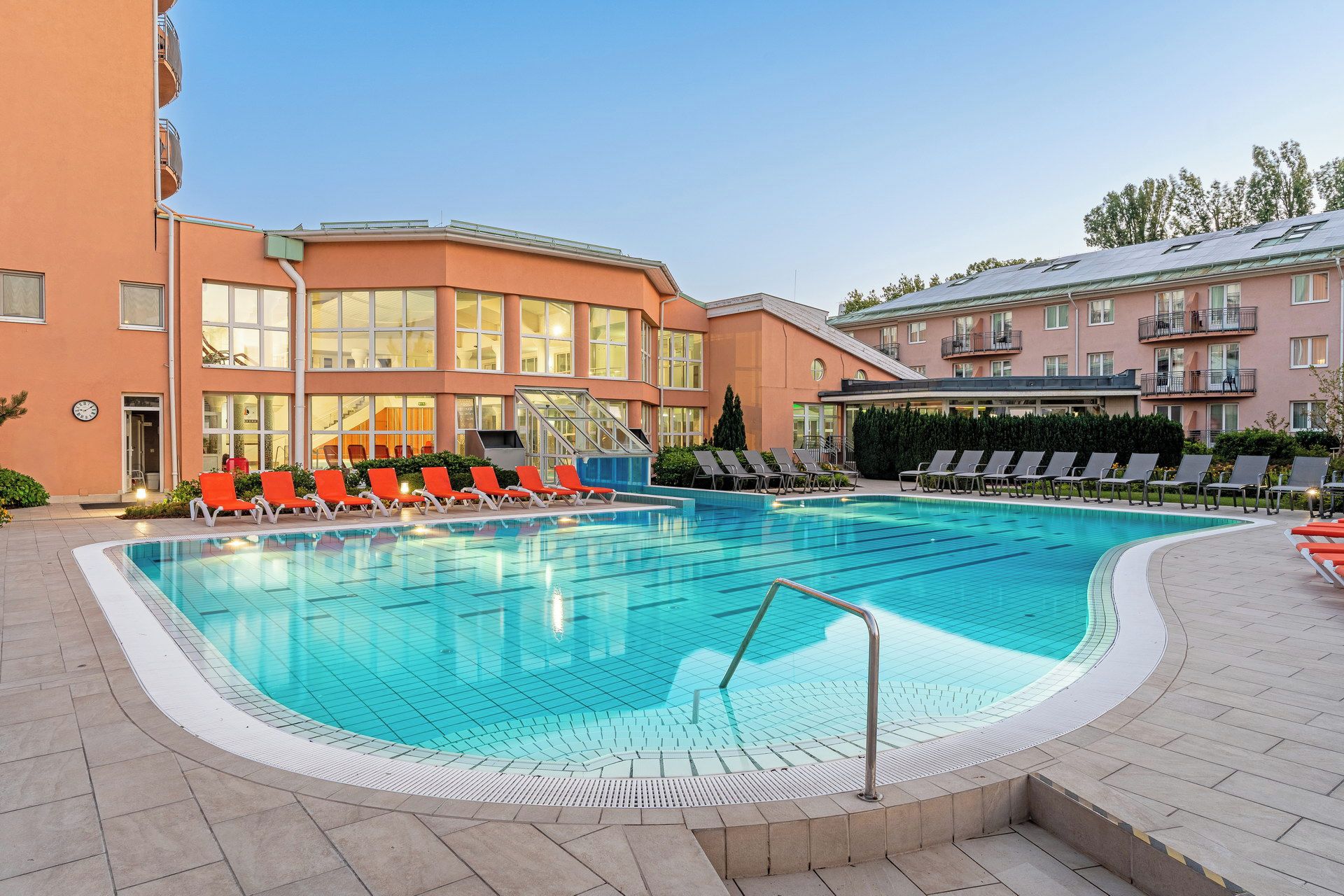 A swimming pool with sun loungers and a building with balconies in the background.
