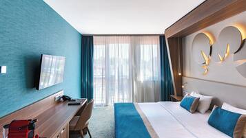 A hotel room with a bed, a desk, a coffee machine, a TV, and a large window with curtains.