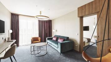 A modern hotel room with a sofa, a desk, a hanging chair, and a large window with curtains.