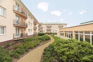 Un edificio residencial de varios pisos con balcones, un jardín ajardinado y un cielo despejado.
