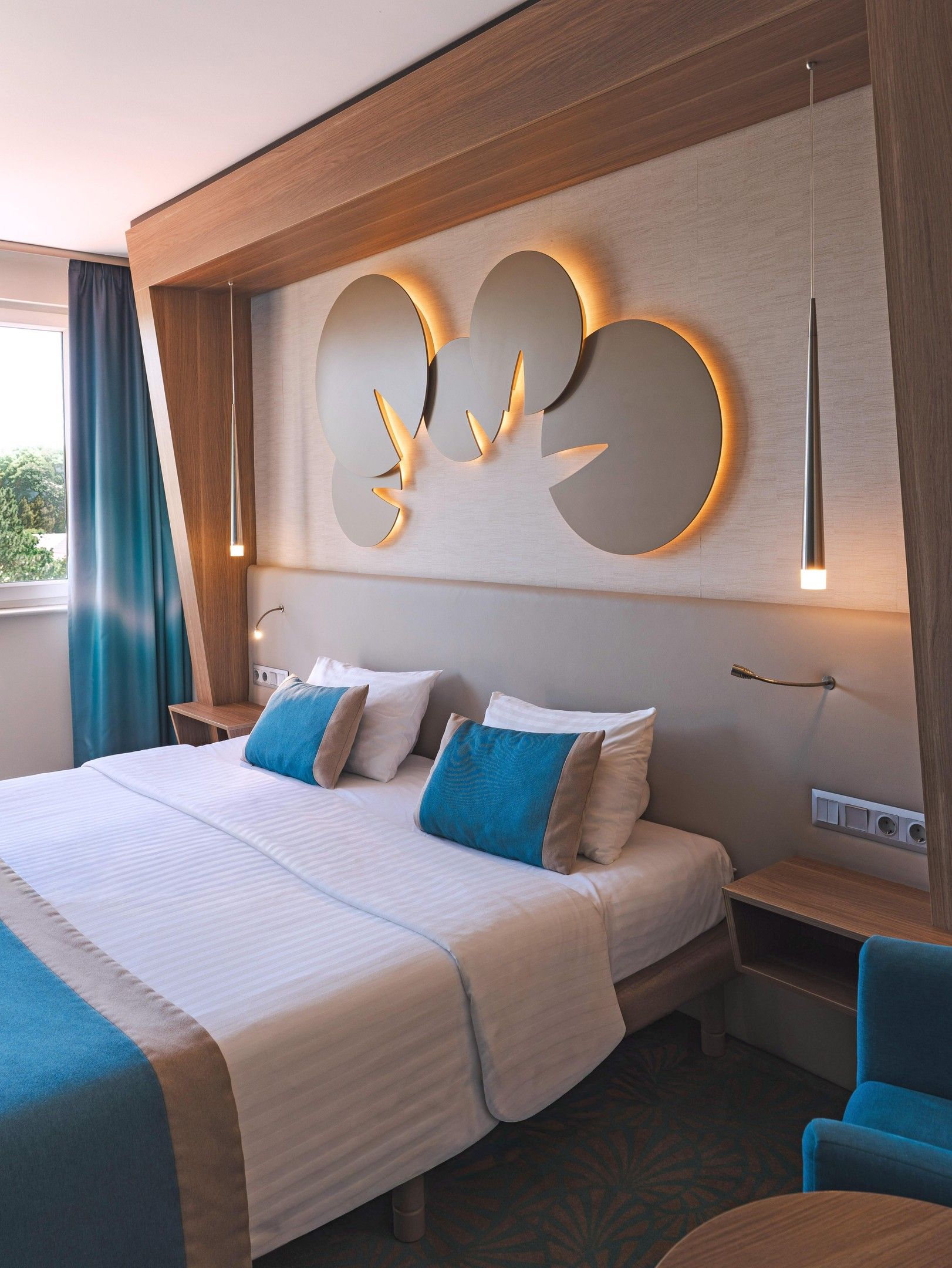 Quarto de hotel com uma cama grande, luminária na parede e vista para o exterior.