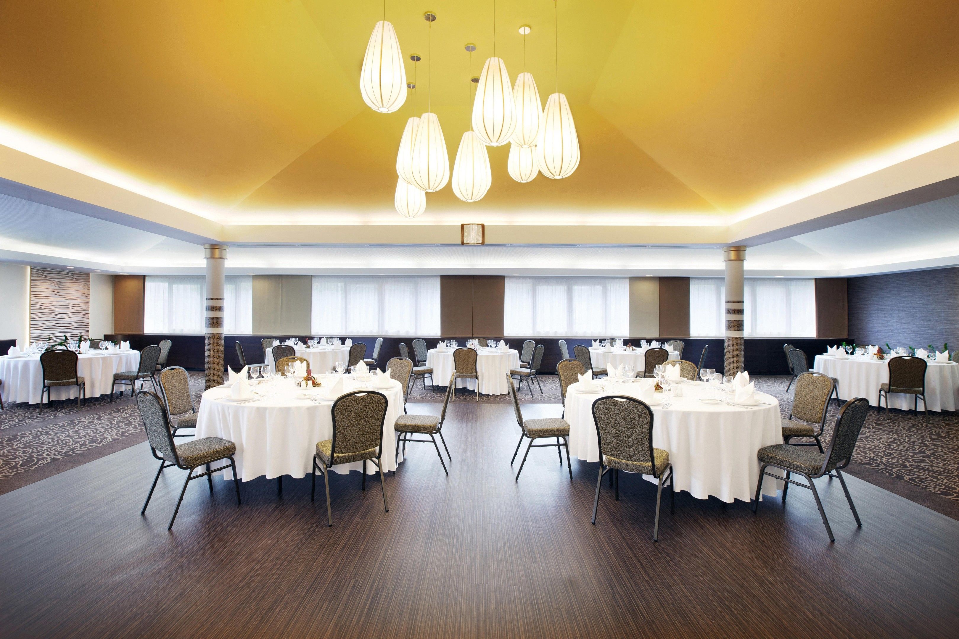 Un gran saló de banquets amb taules rodones, cadires i un llum modern.